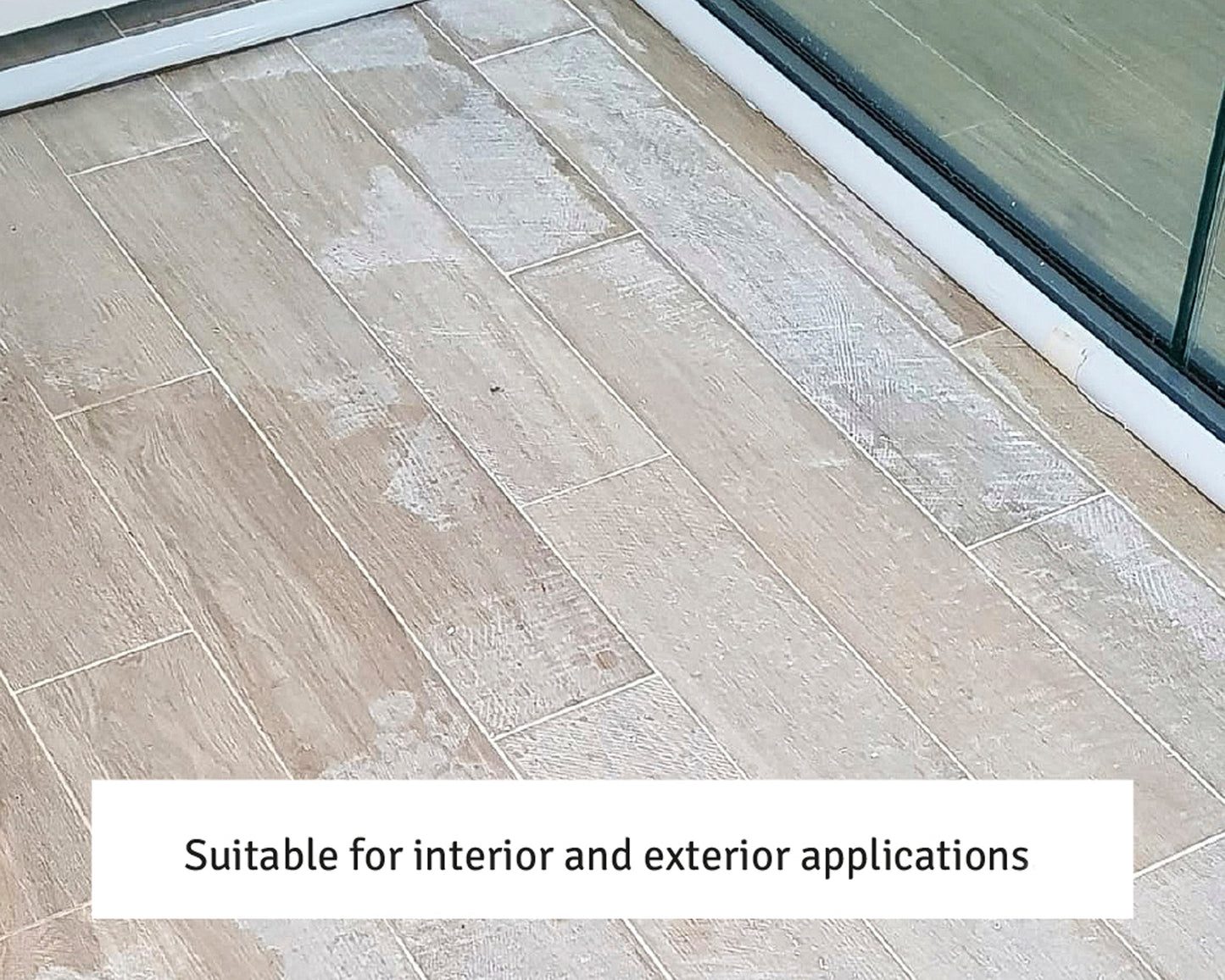 Beige ceramic floor tiles with a wood-like texture installed next to a glass window. The caption reads, "Suitable for interior and exterior applications—use a grout residue remover for a pristine finish.