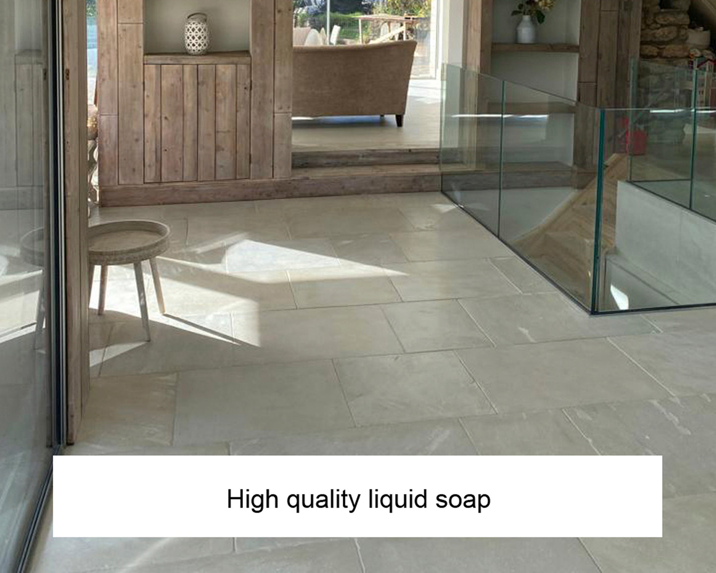 A modern, sunlit room with light stone tile flooring, wooden furniture, glass panels, and a stool. The text "High quality liquid soap and stone surface cleaner" appears at the bottom of the image.