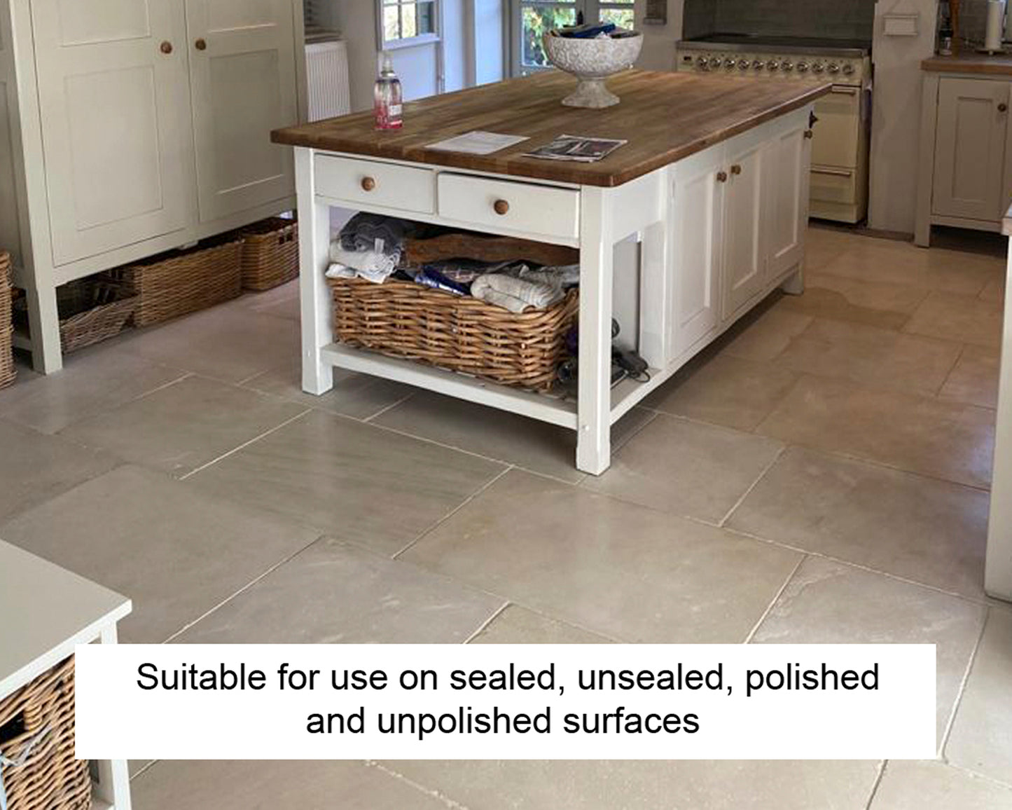 A bright kitchen with a wooden-topped island and wicker baskets underneath. The floor is light-colored stone tiles. Text reads: "Stone surface cleaner suitable for use on sealed, unsealed, polished and unpolished surfaces.