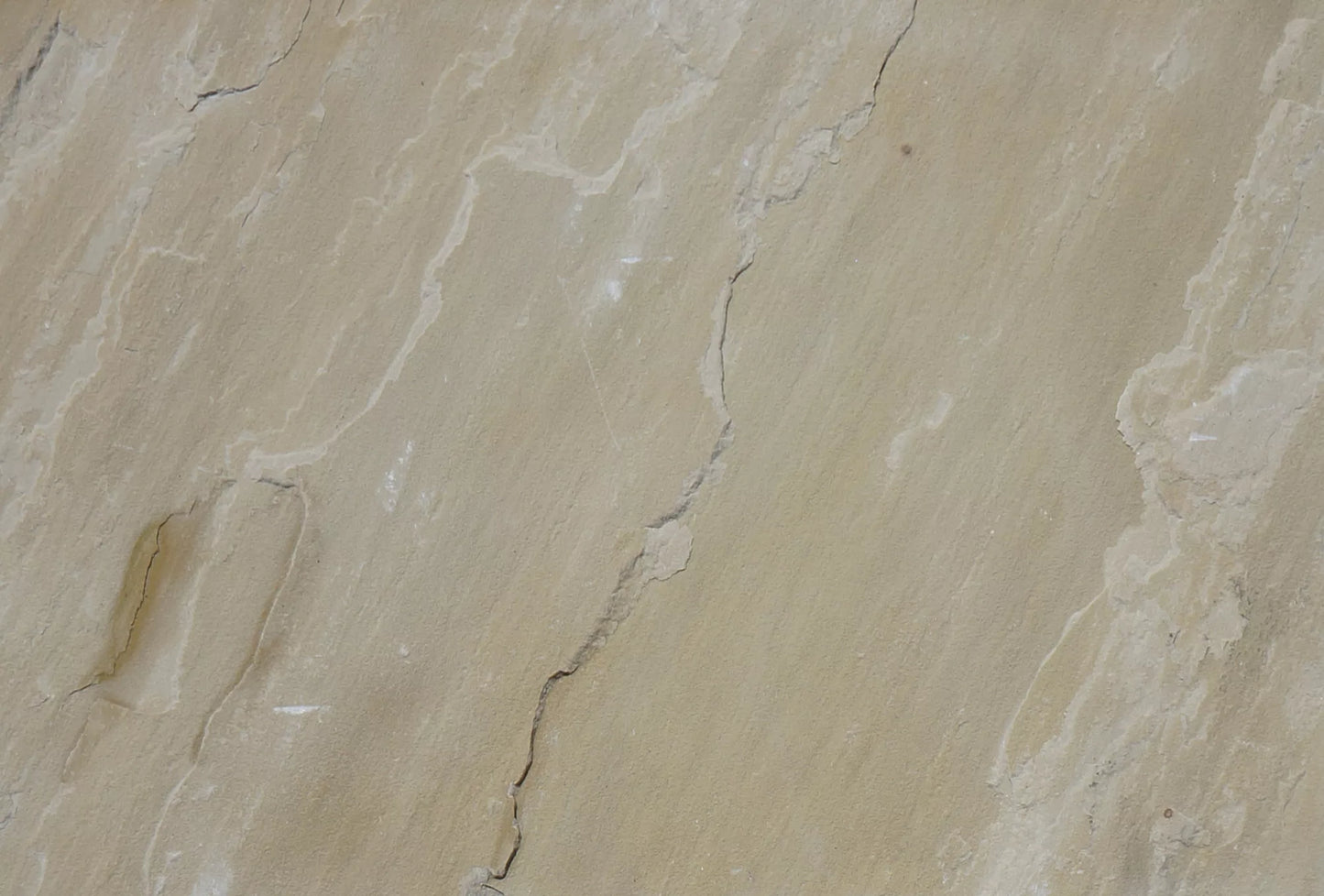 Close-up view of a beige Mint Sandstone Paving surface with natural cracks and textured lines running across it, showing subtle color variations and uneven patterns typical of quality paving tiles.