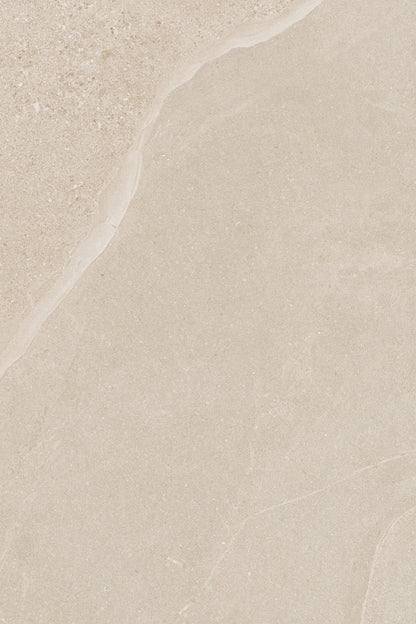 A close-up of Ashmore Ivory Porcelain Paving Slabs showcases a beige surface with subtle variations in texture and color, featuring smooth areas and a slightly rough, natural pattern along the top edge.