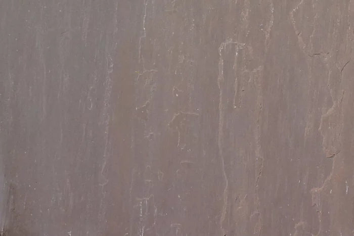 Close-up of an Autumn Brown Sandstone Paving surface, showcasing smooth, brownish-grey sandstone slabs with subtle vertical streaks and faint natural texture patterns.