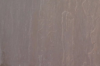 Close-up of an Autumn Brown Sandstone Paving surface, showcasing smooth, brownish-grey sandstone slabs with subtle vertical streaks and faint natural texture patterns.