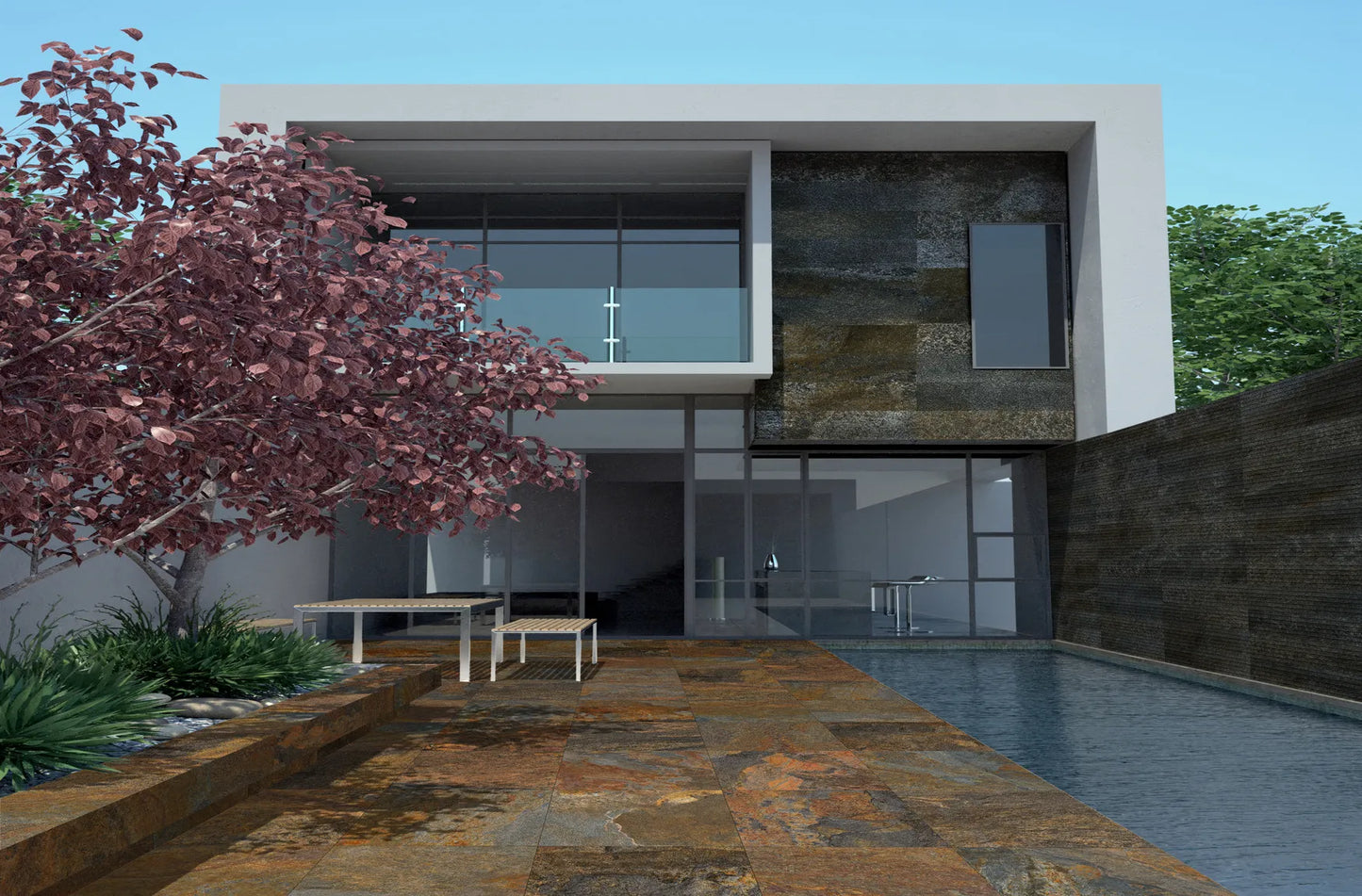 Modern two-story house with large glass windows, a patio with slip-resistant paving tiles, a pool on the right, a small table and chairs, a pink-leaved tree on the left, and greenery in the background under a clear sky.