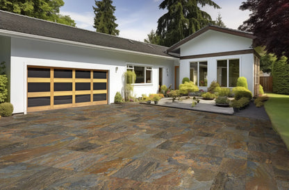 A modern house with a wooden garage door, large windows, and a front yard featuring Cartier Moon Porcelain tiles—slip-resistant paving tiles that beautifully complement the well-maintained shrubs and plants under clear skies.