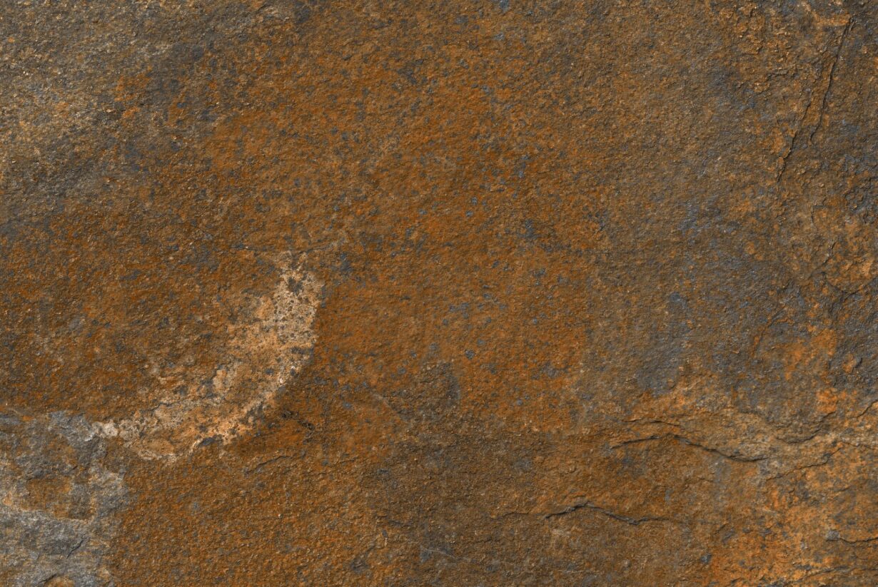 Close-up view of a rough, brown and dark gray stone surface with a textured, uneven appearance and natural color variations, reminiscent of outdoor porcelain tiles for slip-resistant paving.