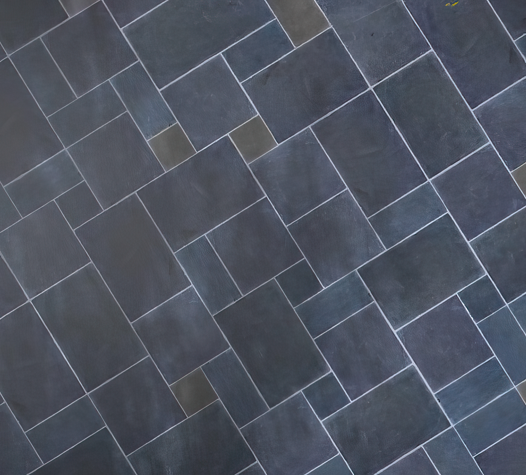 A geometric pattern of rectangular paving tiles, arranged in a staggered, interlocking layout with visible white grout lines. The tiles, reminiscent of garden stepping stones, vary slightly in shade for a subtly textured appearance.