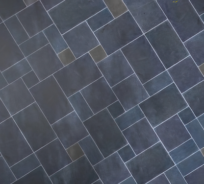 A geometric pattern of rectangular paving tiles, arranged in a staggered, interlocking layout with visible white grout lines. The tiles, reminiscent of garden stepping stones, vary slightly in shade for a subtly textured appearance.