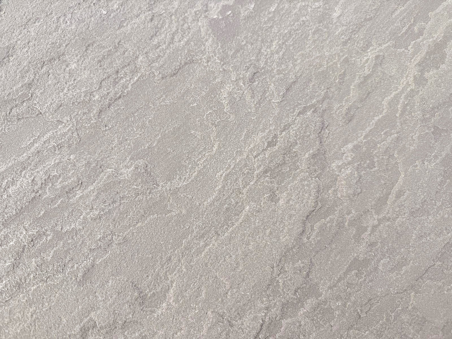 A close-up view of a textured, light grey surface with irregular, wavy patterns and subtle shading variations, resembling Kandla Grey Sandstone Paving or natural sandstone slabs.