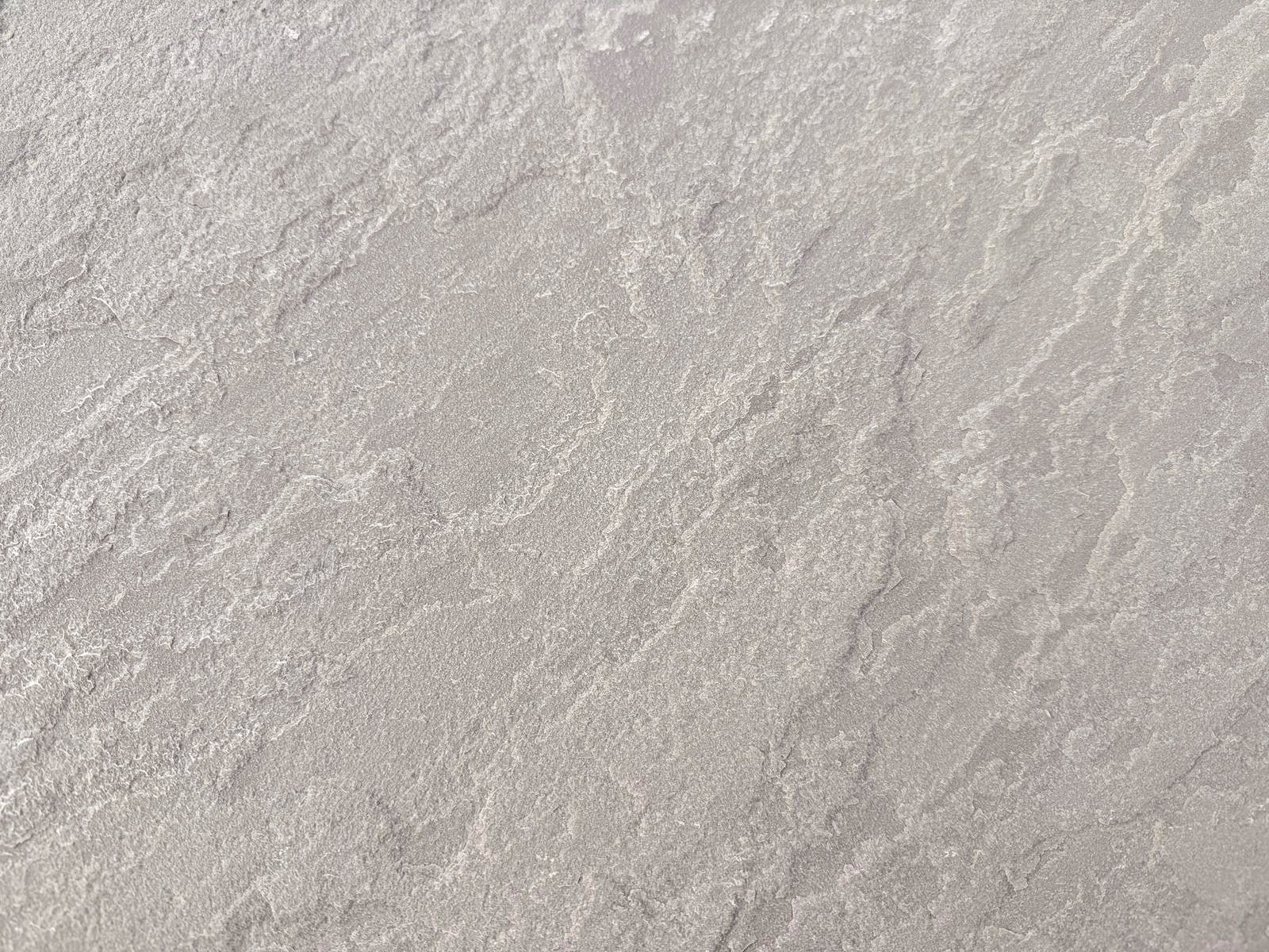 A close-up view of a textured, light grey surface with irregular, wavy patterns and subtle shading variations, resembling Kandla Grey Sandstone Paving or natural sandstone slabs.