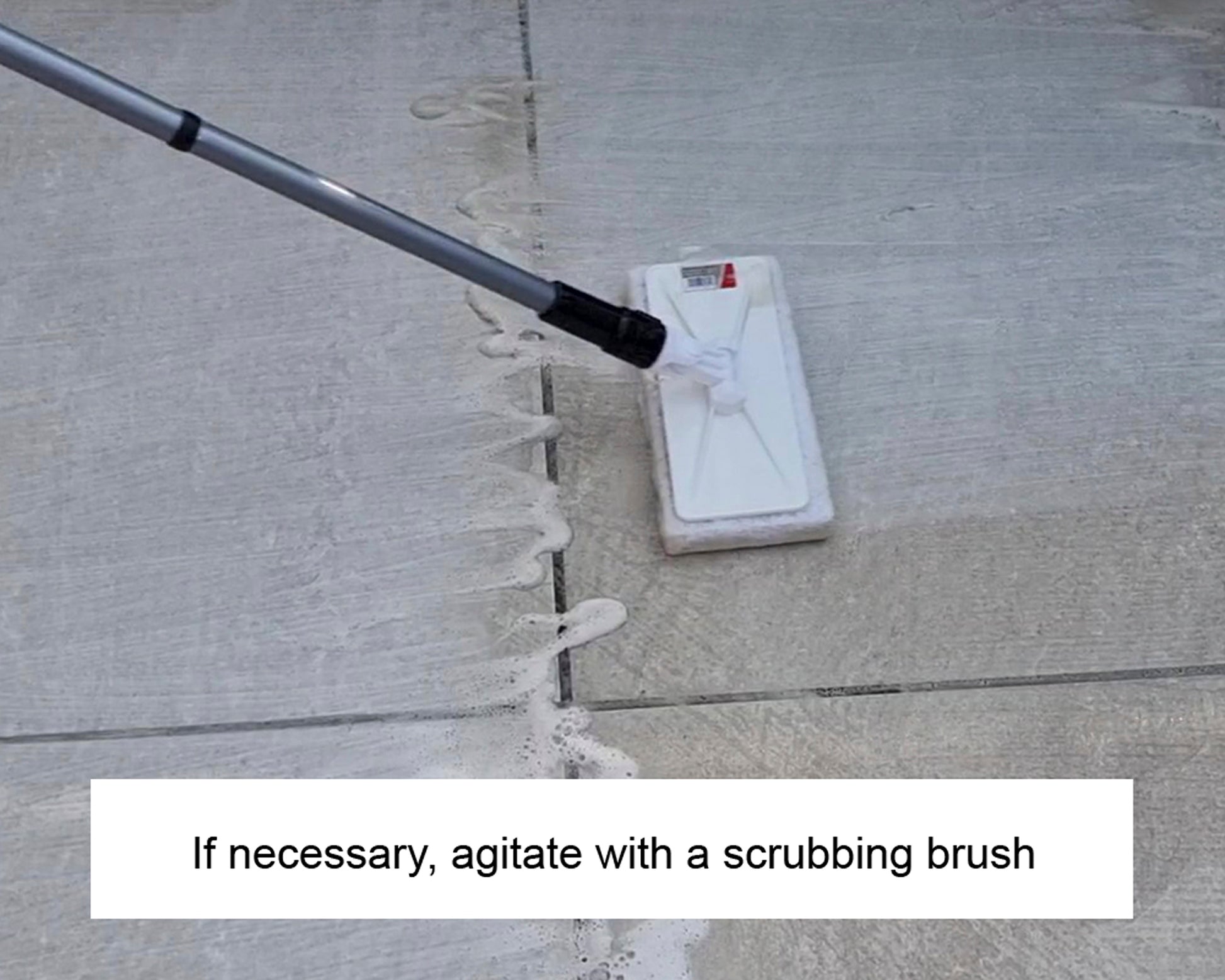 A scrubbing brush with a long handle is being used to clean soapy residue off an outdoor concrete surface. Text below reads, "If necessary, agitate with a scrubbing brush and stone cleaner.