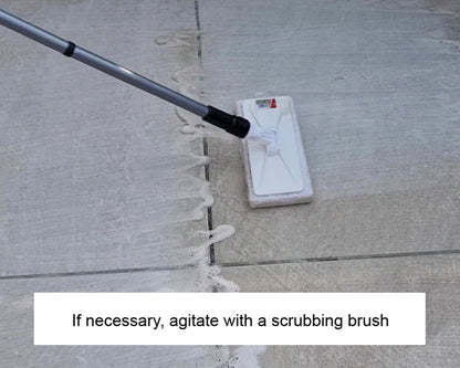 A scrubbing brush with a long handle is being used to clean soapy residue off an outdoor concrete surface. Text below reads, "If necessary, agitate with a scrubbing brush and stone cleaner.