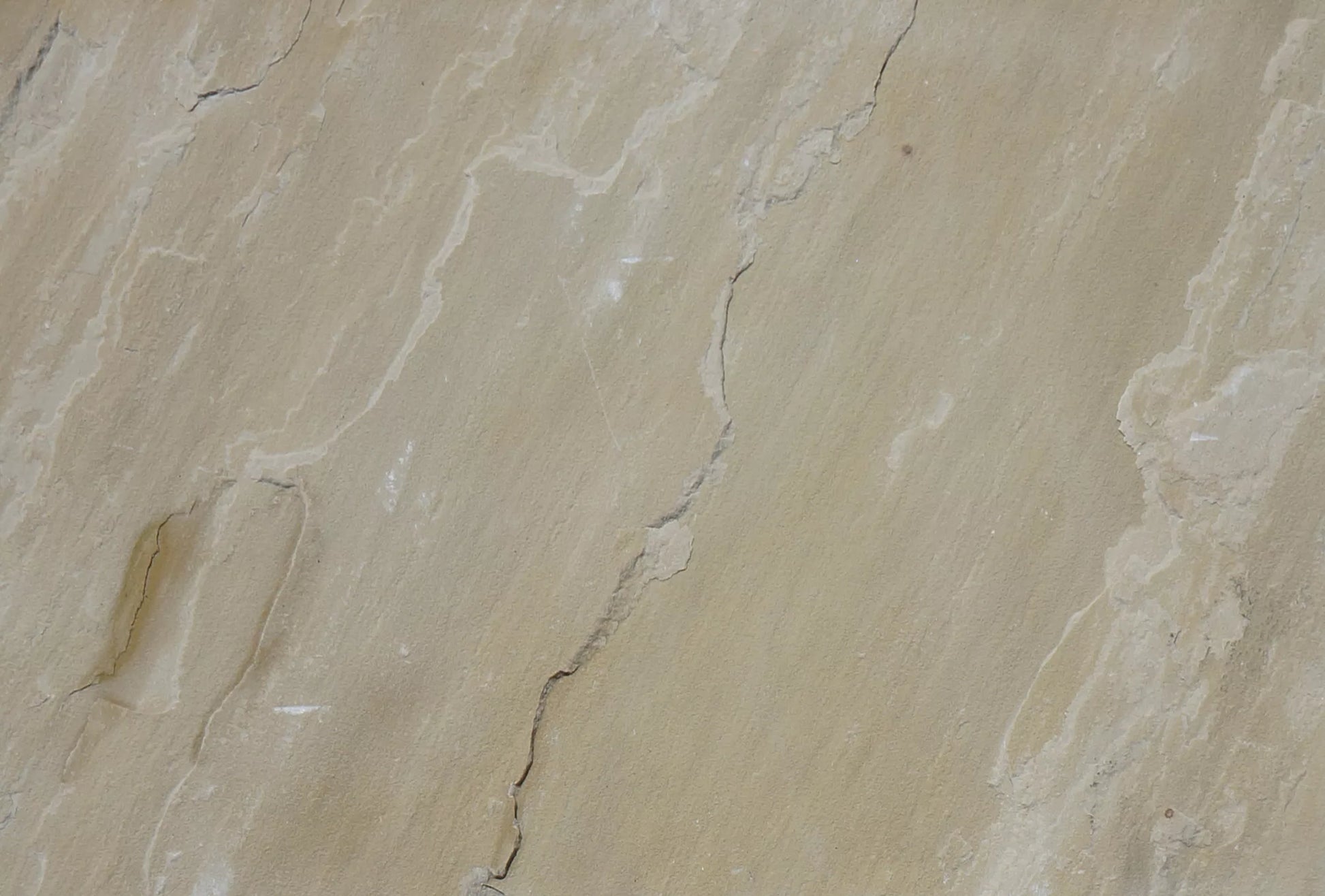 Close-up view of a beige Mint Sandstone Paving surface with natural cracks and textured lines running across it, showing subtle color variations and uneven patterns typical of quality paving tiles.