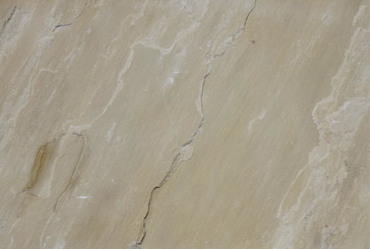 Close-up view of a beige Mint Sandstone Paving surface with natural cracks and textured lines running across it, showing subtle color variations and uneven patterns typical of quality paving tiles.