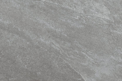 Gray stone surface with subtle natural texture and light veining, creating a slightly rough, matte appearance. Rasa Grigio Porcelain tiles offer slip-resistant paving perfect for outdoor spaces, with blended shades of lighter and darker gray.