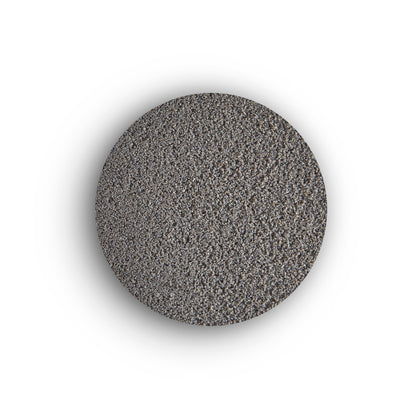 A circular mound of fine, gray granular material is centered on a white background, resembling sand or the texture of brush-in jointing solution used for external tile grout.